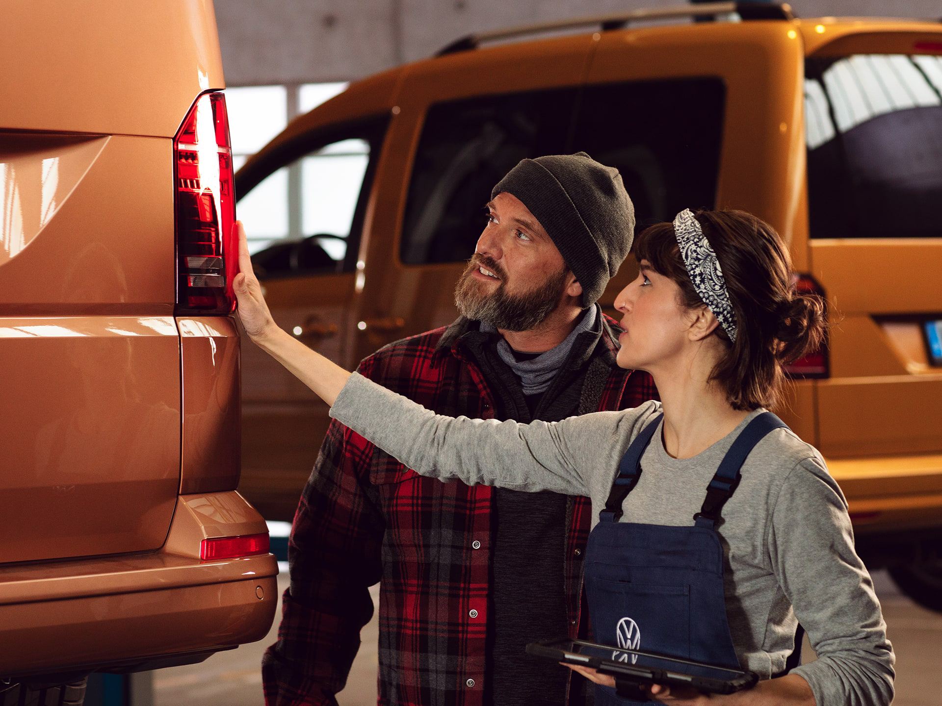 Due addetti al lavoro ispezionano i proiettori posteriori di un veicolo commerciale Volkswagen.